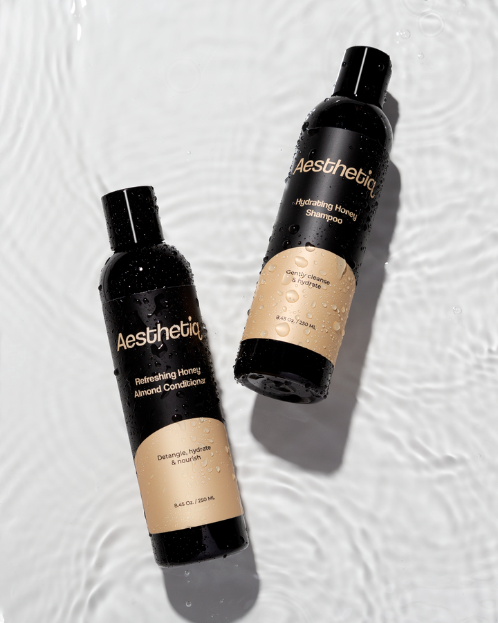 Black shampoo and conditioner bottles with water droplets on a rippling surface.